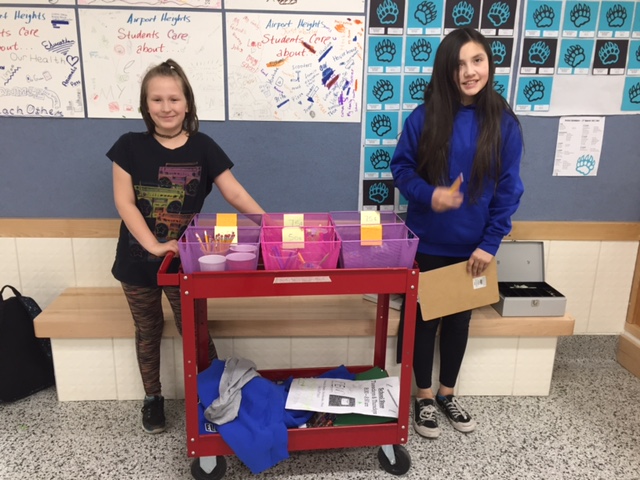 Two girls standing next to a sales cart of school supplies.